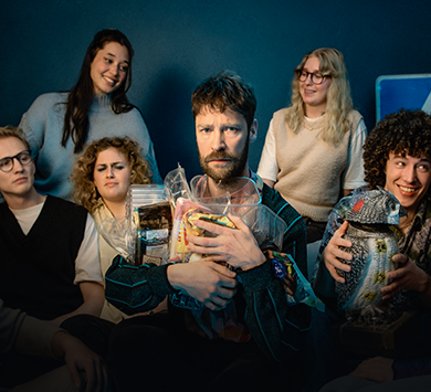 Styrbjörn sitter omringad av flera glada männsiskor medan han håller hårt i sina plastförpackningar.