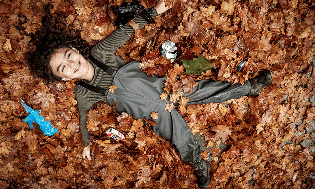 En pojke i lövhög omringad av skräp.