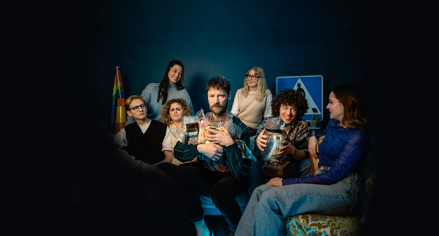 Styrbjörn sitter omringad av flera glada männsiskor medan han håller hårt i sina plastförpackningar.