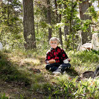 En pojke i skogen som sitter omringad av skräp.