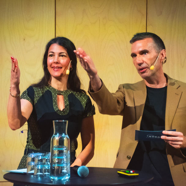 Paulina Luedtke och Rustan gestikulerar på scenen mot något utanför bild.