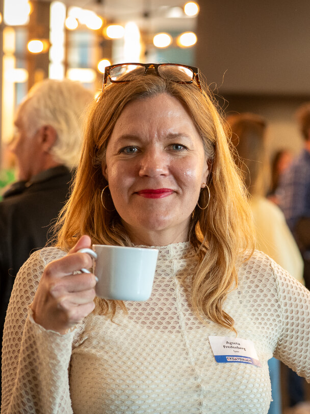 Kvinna som ler med en kopp kaffe i handen.